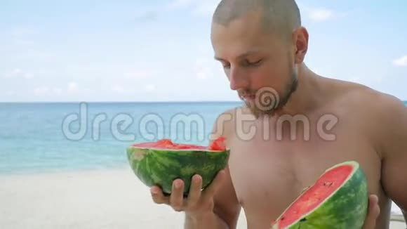 在海滩上吃美味的西瓜的年轻英俊的大胡子泰国范甘高清慢速运动视频的预览图