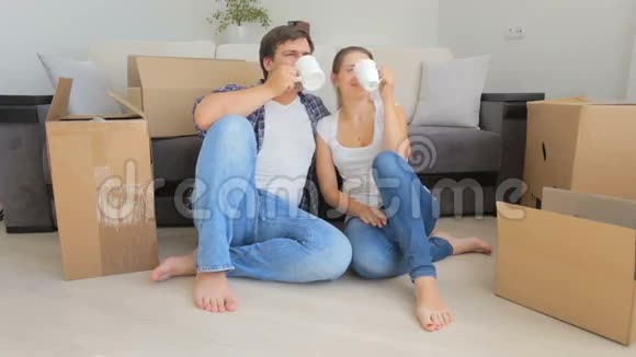 快乐的年轻夫妇在新家拆箱时一边喝咖啡一边休息视频的预览图