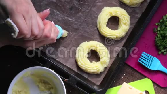 一个女人在烤盘上形成土豆泥戒指借助糕点包旁边的其他烹饪原料视频的预览图