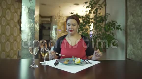 美丽的中年黑发女人穿着红色连衣裙独自一人在高档餐厅用筷子吃食物视频的预览图