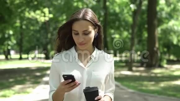 女人在公园里喝咖啡检查手机视频的预览图