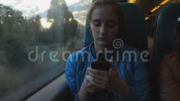 年轻的黑发时髦女孩使用智能手机坐在火车的窗户附近视频的预览图