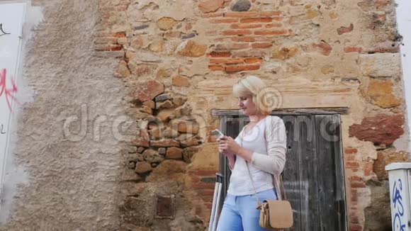 一位年轻女子在西班牙欧洲中世纪古城的狭窄小巷里使用智能手机视频的预览图