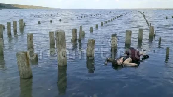 身体细长的金发碧眼穿着泥和湿衣服躺在河口靠近被摧毁的盐池的木柱视频的预览图