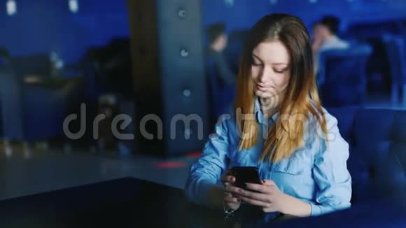 一个年轻女子独自坐在咖啡馆或夜总会里用电话视频的预览图