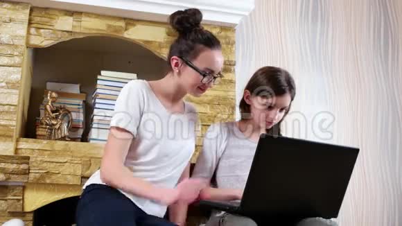 戴眼镜的女孩看着妹妹在笔记本电脑上做作业十几岁的女孩坐在一起视频的预览图