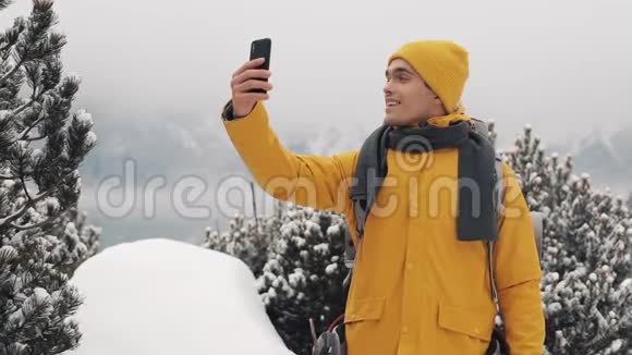 英俊的徒步旅行者在智能手机上打电话对着相机挥手微笑着和朋友说话美丽的冬天视频的预览图