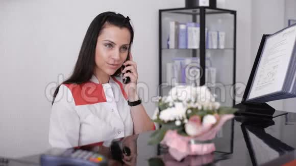 一位美丽的微笑护士在办公桌站边打电话的肖像视频的预览图