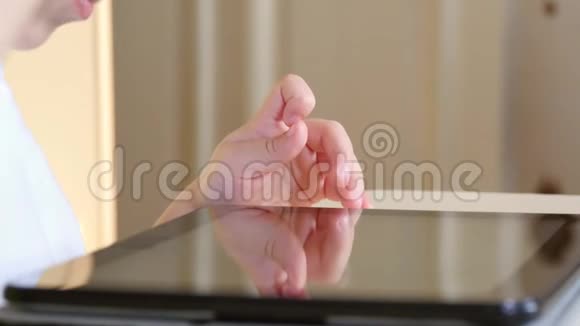 坐在桌子旁的小男孩摸着平板电脑的触摸屏一个孩子在玩平板电脑正在微笑视频的预览图