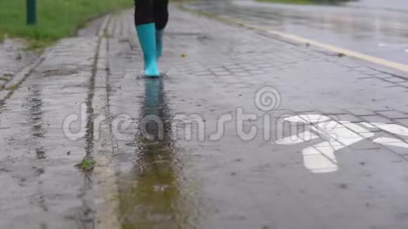 穿着蓝色橡胶靴的女人在水坑上跳跃的特写镜头视频的预览图
