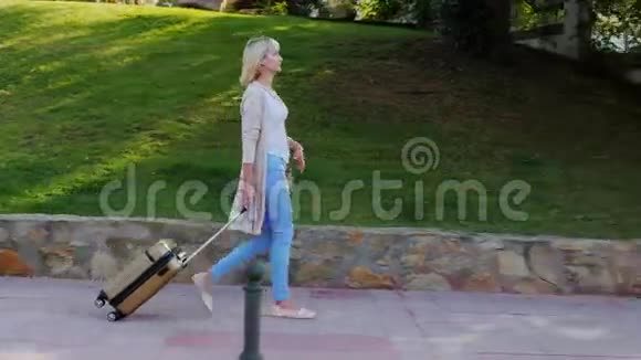 带着旅行袋的女人沿着度假区域走在晴朗的晴天视频的预览图