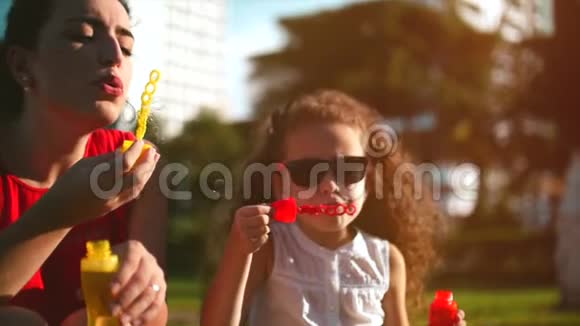 快乐的妈妈和孩子在公园里吹肥皂泡慢动作库存录像慢动作视频的预览图
