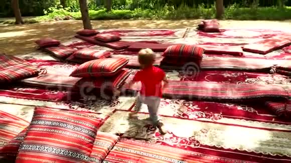 有趣的小男孩在公园里用地毯和床垫奔跑和欢乐视频的预览图
