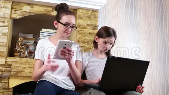 年长的女孩帮助她的妹妹在笔记本电脑上做作业女孩坐在地毯上视频的预览图