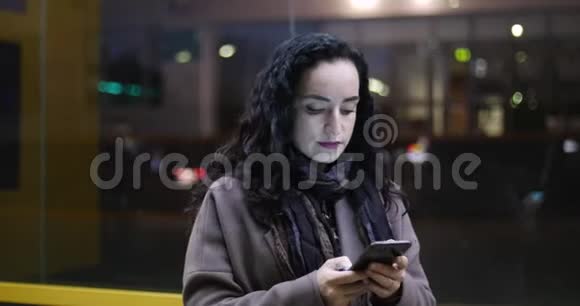 有魅力的女人在夜晚城市的节日灯光的背景下一边使用手机一边穿过街道视频的预览图