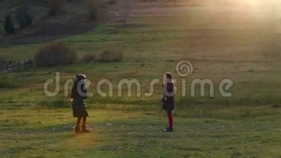 两个美丽的小女孩在夕阳下的秋天在大自然上玩球视频的预览图