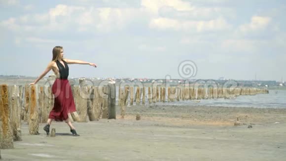 美丽的金发女郎穿着一件连衣裙斜靠在河口中央的木砖上在一个废弃的盐池里视频的预览图