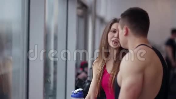 英俊的男人正在和窗户附近一个漂亮的运动女孩说话人们在健身房锻炼后休息视频的预览图