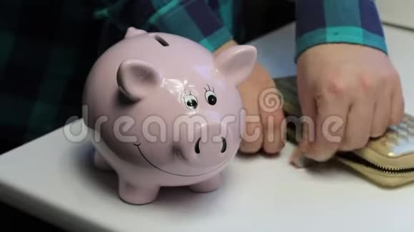 桌子上有一只粉红色的猪形的储蓄罐散落的硬币一个人从桌子上收集硬币然后把视频的预览图