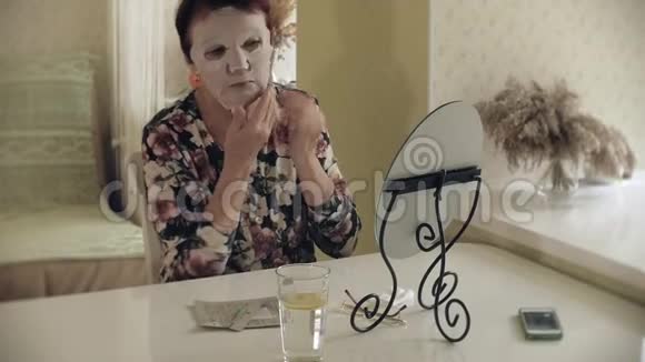 一位老妇人照镜子把化妆织物面具戴在脸上外院护理整形外科和视频的预览图