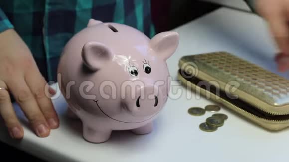 桌子上有一只粉红色的猪形的储蓄罐散落的硬币一个人从桌子上收集硬币然后把视频的预览图
