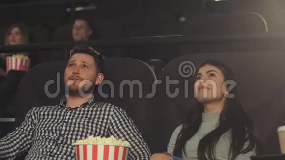 一个有女朋友的年轻人正在电影院看电影吃爆米花视频的预览图