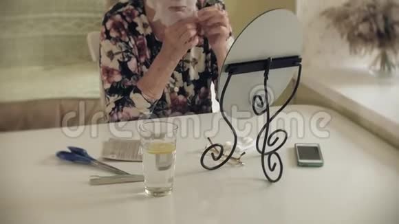 一位老妇人照镜子把化妆织物面具戴在脸上外院护理整形外科和视频的预览图