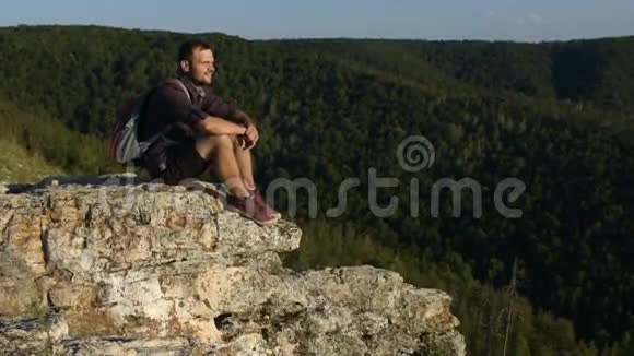 男人坐在悬崖上看着相机微笑着视频的预览图