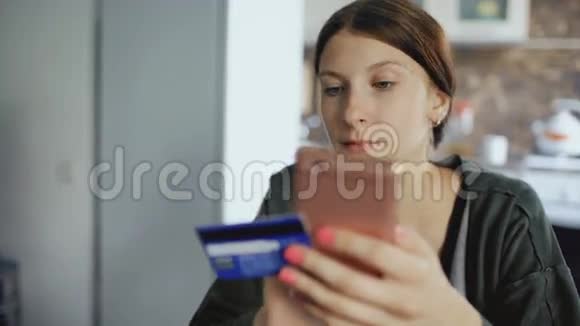 这位美丽的年轻女性的特写镜头使用智能手机和信用卡进行网上银行和购物视频的预览图