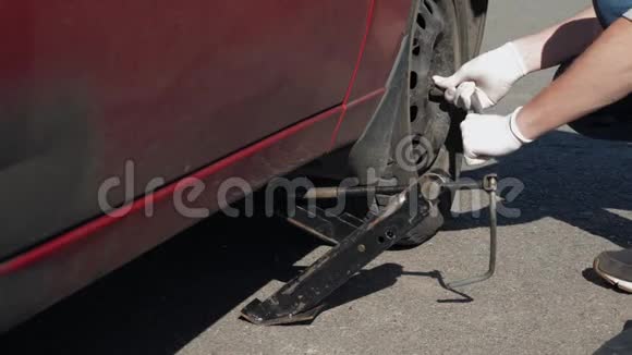 一个戴着白手套的经验不足的人撬开了一辆破而脏的红色汽车试图拧开车轮视频的预览图