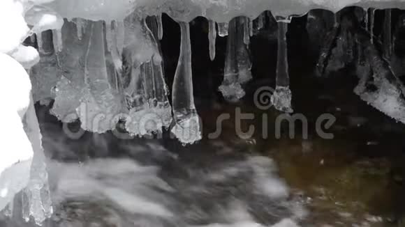 早春寒冷的森林小溪冰雪和长长的冰柱悬在水流中视频的预览图