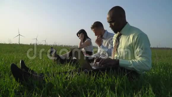 一群穿着商务服的人在阳光明媚的日子里在风力发电机附近工作视频的预览图