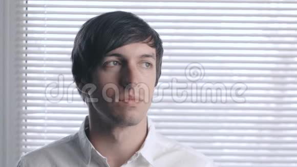 百叶窗背景上一个穿白色衬衫的年轻人的肖像视频的预览图