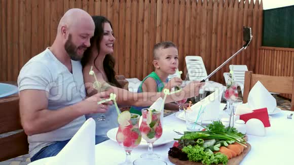 快乐的家庭聚餐在家后院父母带着孩子拍照在智能手机上做自拍坐在那里视频的预览图