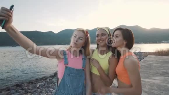 三个朋友的女人微笑着用智能手机拍摄自画像照片视频的预览图