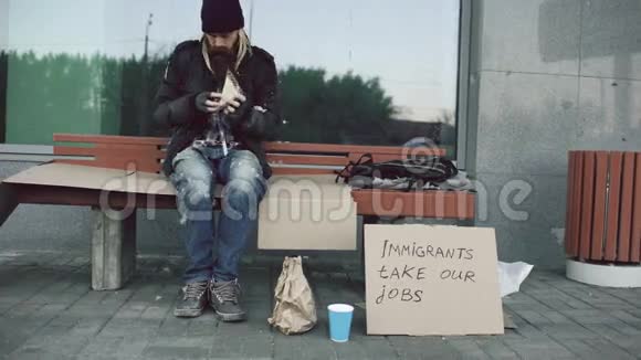 由于移民危机无家可归和失业的欧洲人带着硬纸板标牌在城市大街的长椅上吃三明治视频的预览图