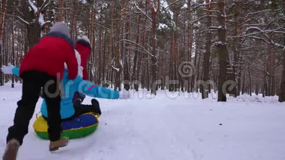 快乐的孩子们骑着他们的母亲在雪橇和一个充气雪管在松林幸福的家庭妈妈和孩子们玩视频的预览图