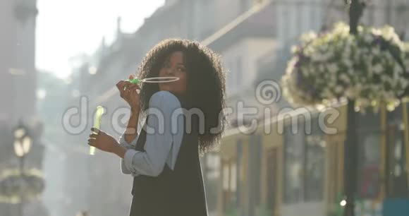 迷人的非洲裔美国女孩在肩膀上吹肥皂泡的侧视街道的位置视频的预览图