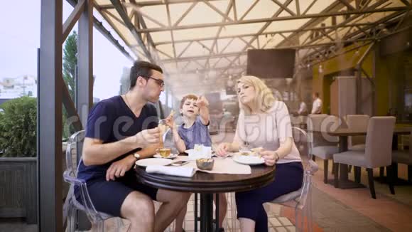 男孩和父母坐在一起在自助餐厅的露台上用餐视频的预览图