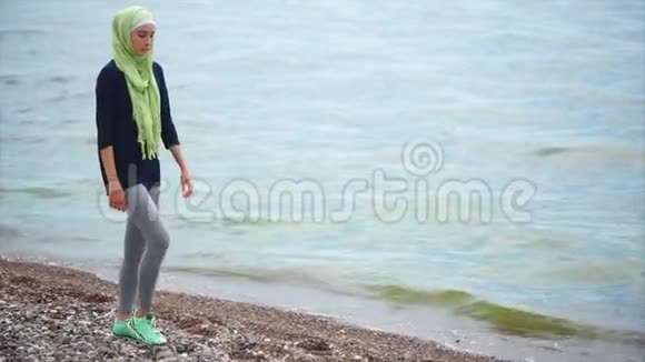 一位戴着面纱的年轻穆斯林妇女带着沉思的目光沿着大海走来视频的预览图