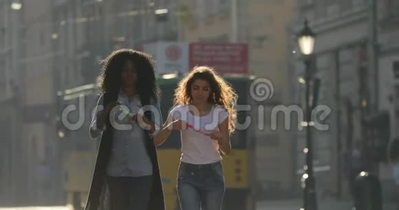 两个快乐的女朋友在市中心散步时吹肥皂泡其中一个是非裔美国人视频的预览图