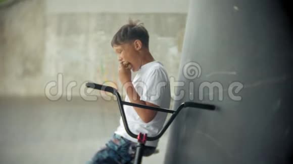 男孩坐在一辆BMX自行车上吃起来有热狗的胃口视频的预览图