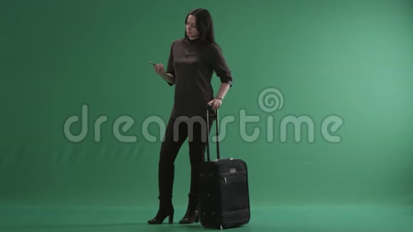 布鲁内特女士拿着行李箱站着用手机说话视频的预览图