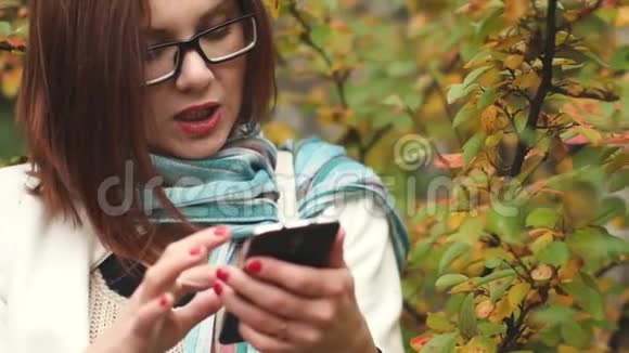 年轻女子在秋天的公园里散步时在一片黄叶背景下在手机上留言视频的预览图