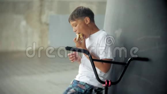 男孩坐在一辆BMX自行车上吃起来有热狗的胃口视频的预览图