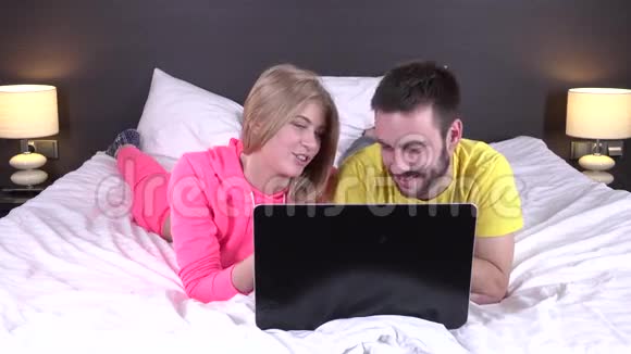 快乐的年轻夫妇躺在床上手提电脑网上购物视频的预览图