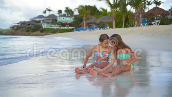 可爱的小女孩在海滩上玩沙子孩子们坐在浅水里做沙堡视频的预览图