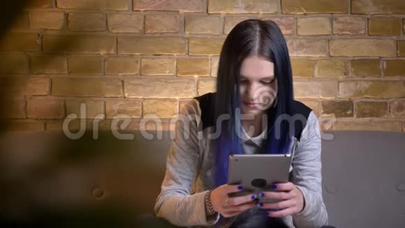 在舒适的公寓里坐在沙发上年轻漂亮的高加索女性在平板电脑上打字的特写镜头视频的预览图