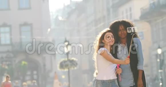 两个微笑的女朋友的视线正在拍摄他们沿街散步的照片他们用的是自拍棒视频的预览图