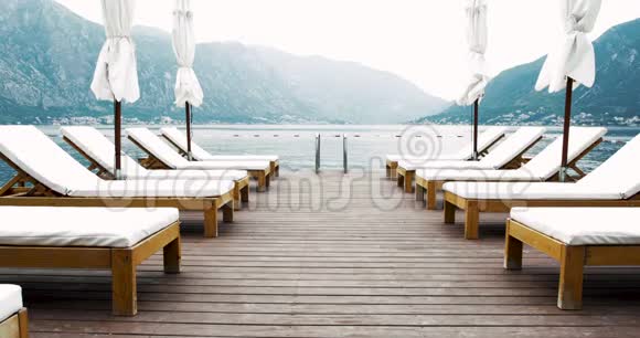 木制码头配有甲板椅和太阳伞环绕着群山是的暑假度假4k视频背景视频的预览图